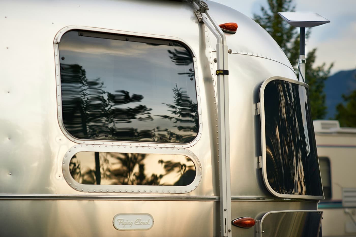 Polished silver Airstream reflecting trees and evening light